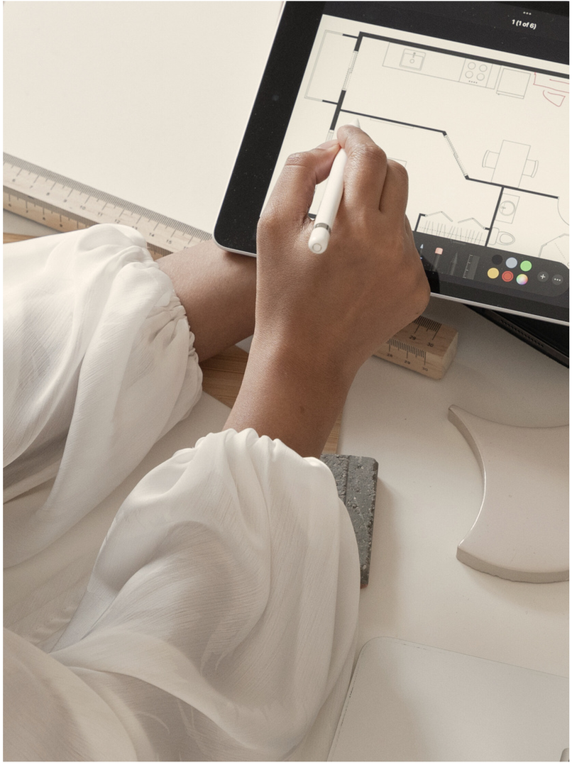 Mano dibujando planos en una tablet sobre escritorio